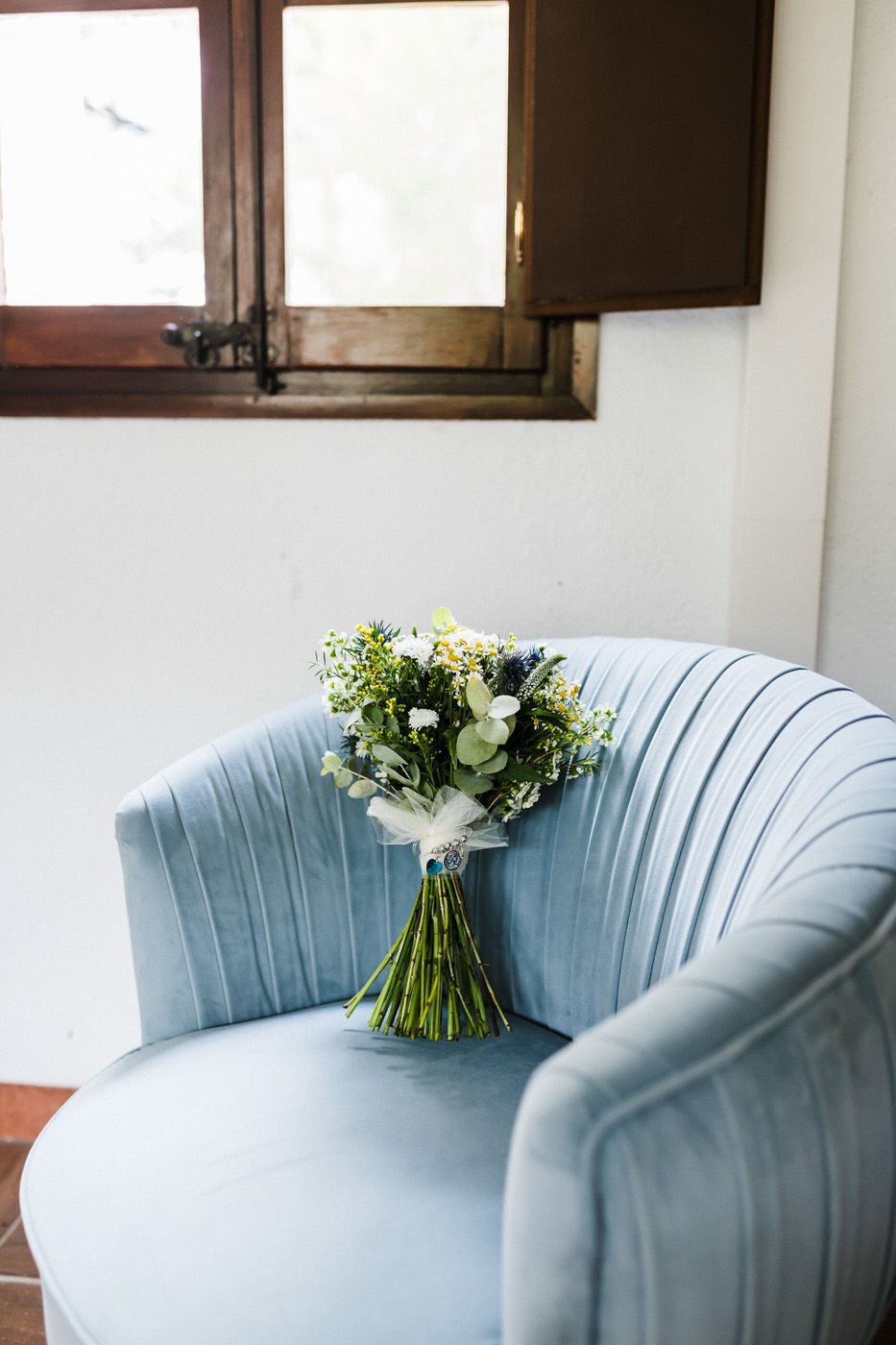 A light blue velvet chair holds a fresh bouquet of white and green flowers.
