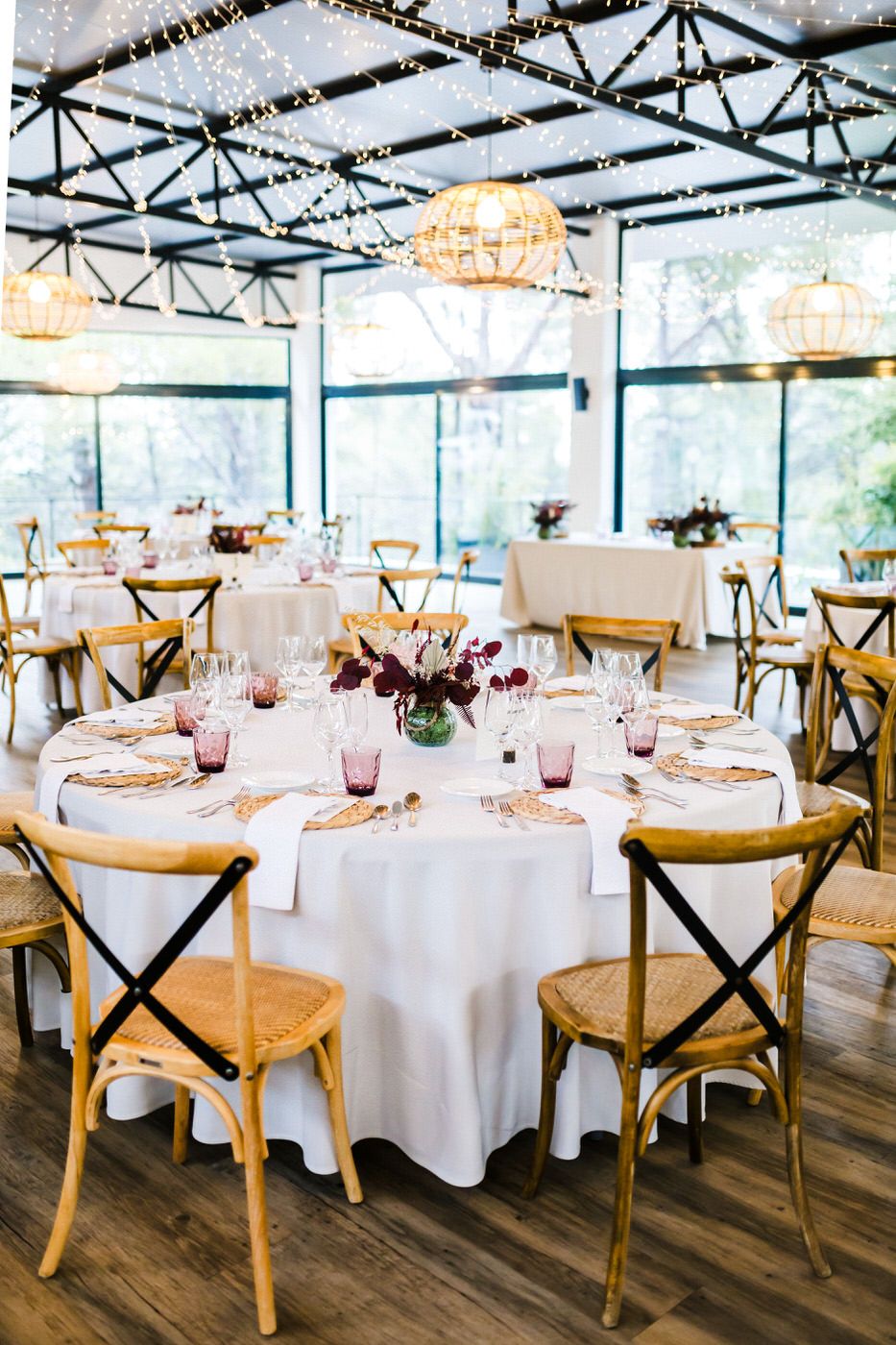 Elegant wedding reception setup with round tables, white linens and pendant lights in a bright venue.