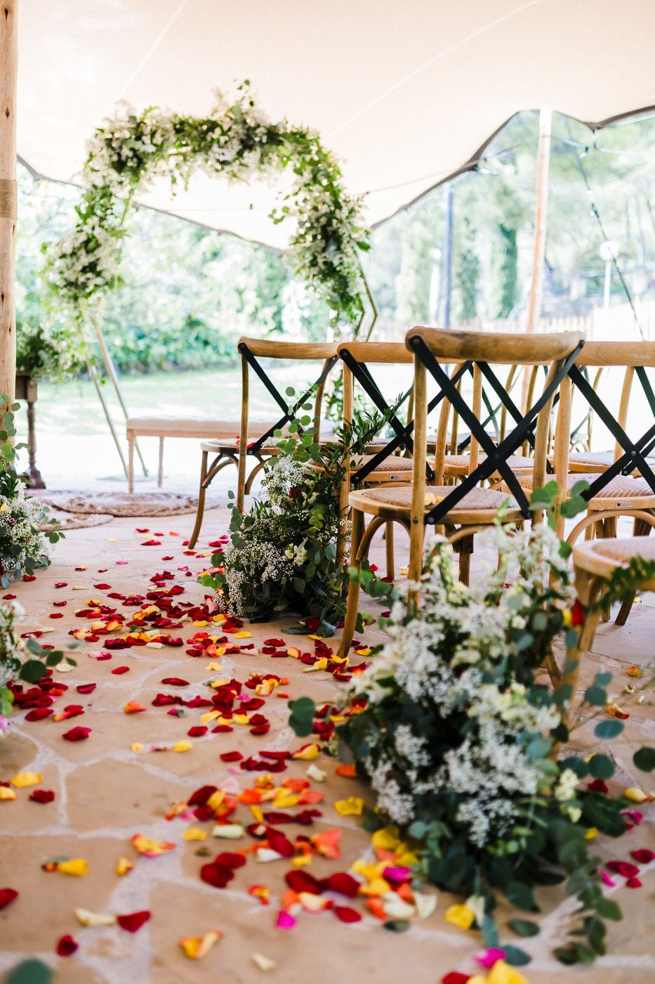 Wedding tent interior decorated with scattered rose petals and floral arrangements on a rustic floor.