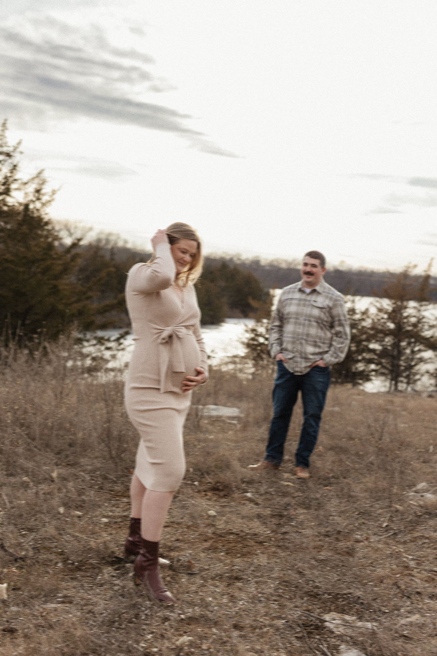 pregnant mother holds baby bump while dad admires her in front of lake olathe during photo session as date night ideas in kansas city