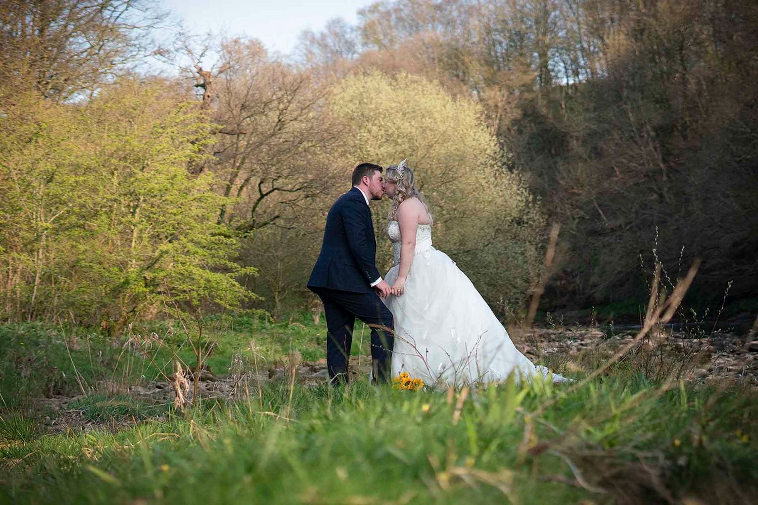 A couple in wedding attire shares romantic moments together in a lush wooded setting during their special day.