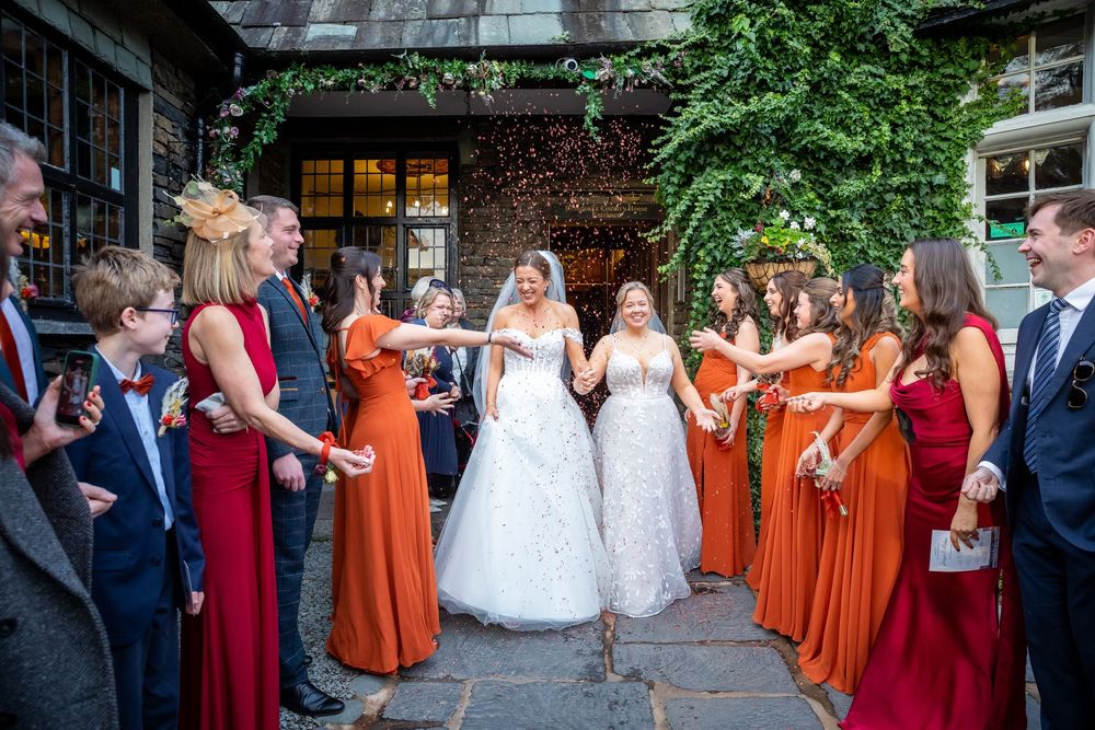 Two brides exit venue hand in hand as guests shower them with confetti in celebration.