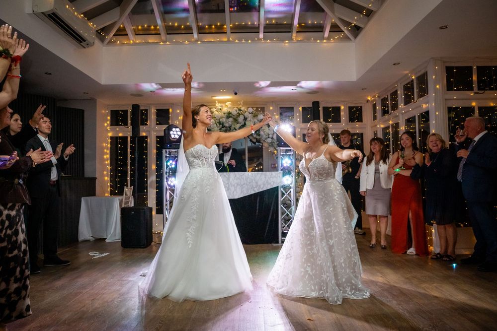 Two brides share their first dance together in an elegant fairy-light decorated reception venue.
