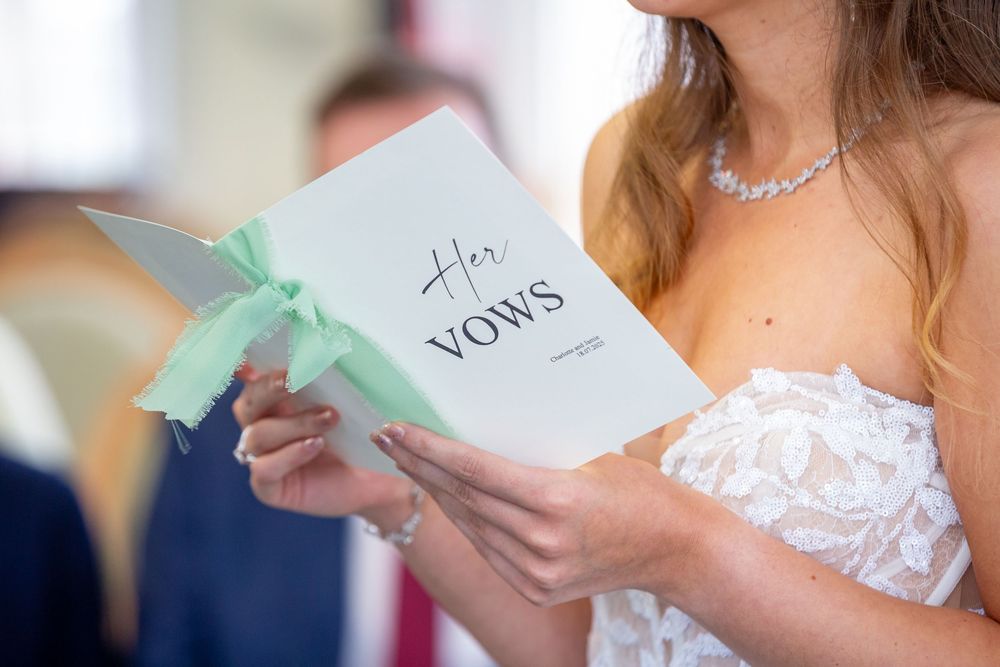 Bride holding elegant white vow booklet with mint green ribbon during wedding ceremony.