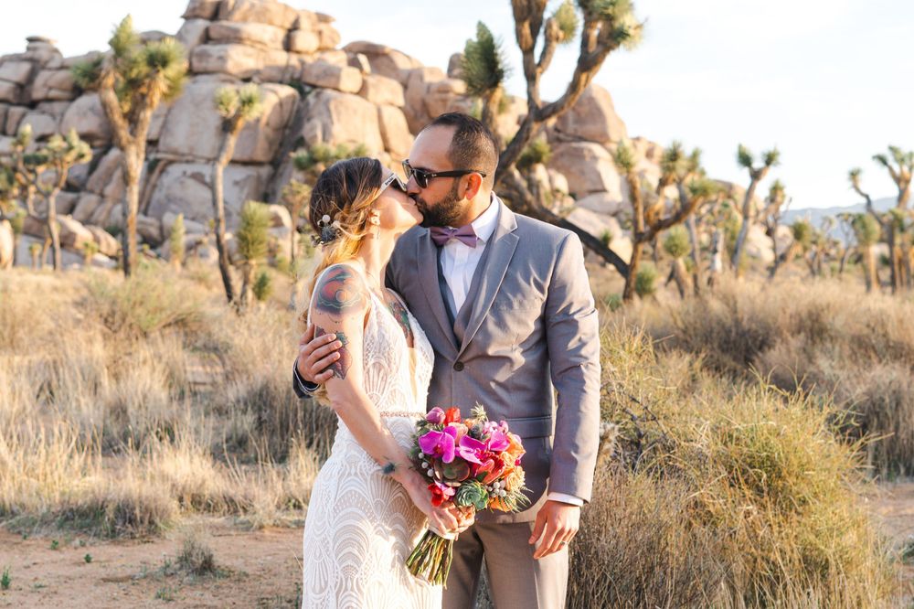 A couple shares romantic moments among desert Joshua trees at sunset in a desert landscape.