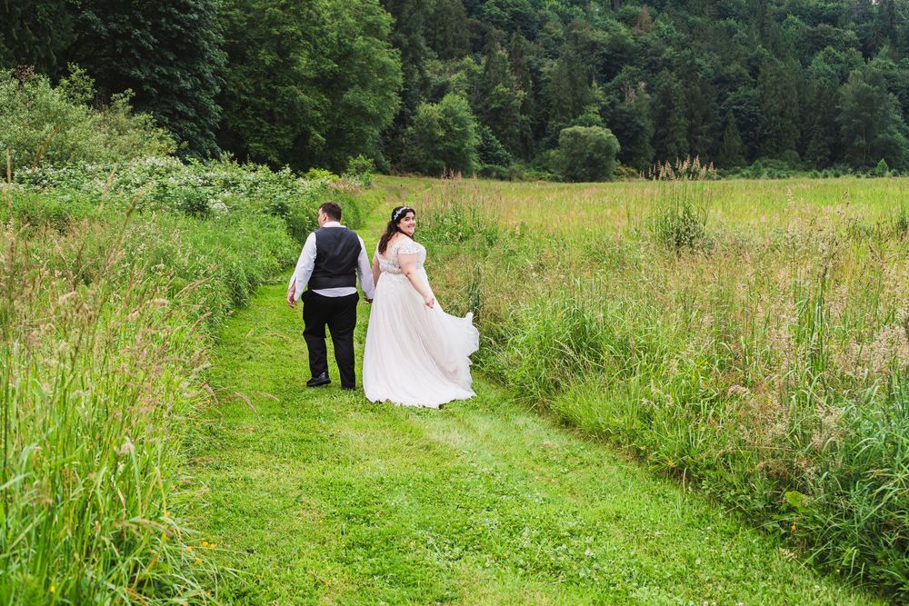 Wedding party walking through a lush green meadow surrounded by trees and natural scenery.