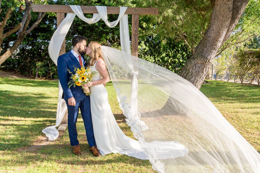 A flowing white wedding veil catches the breeze in a sunlit garden setting during a romantic photo session.