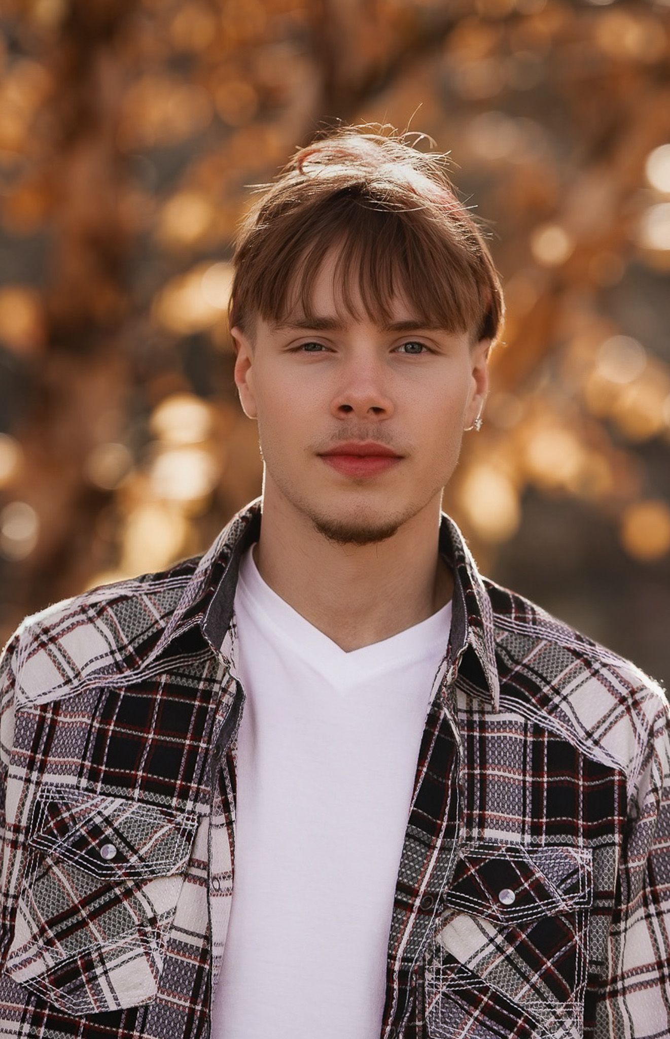 Close-up portrait shot wearing plaid jacket and white shirt against autumn background with bokeh effect.