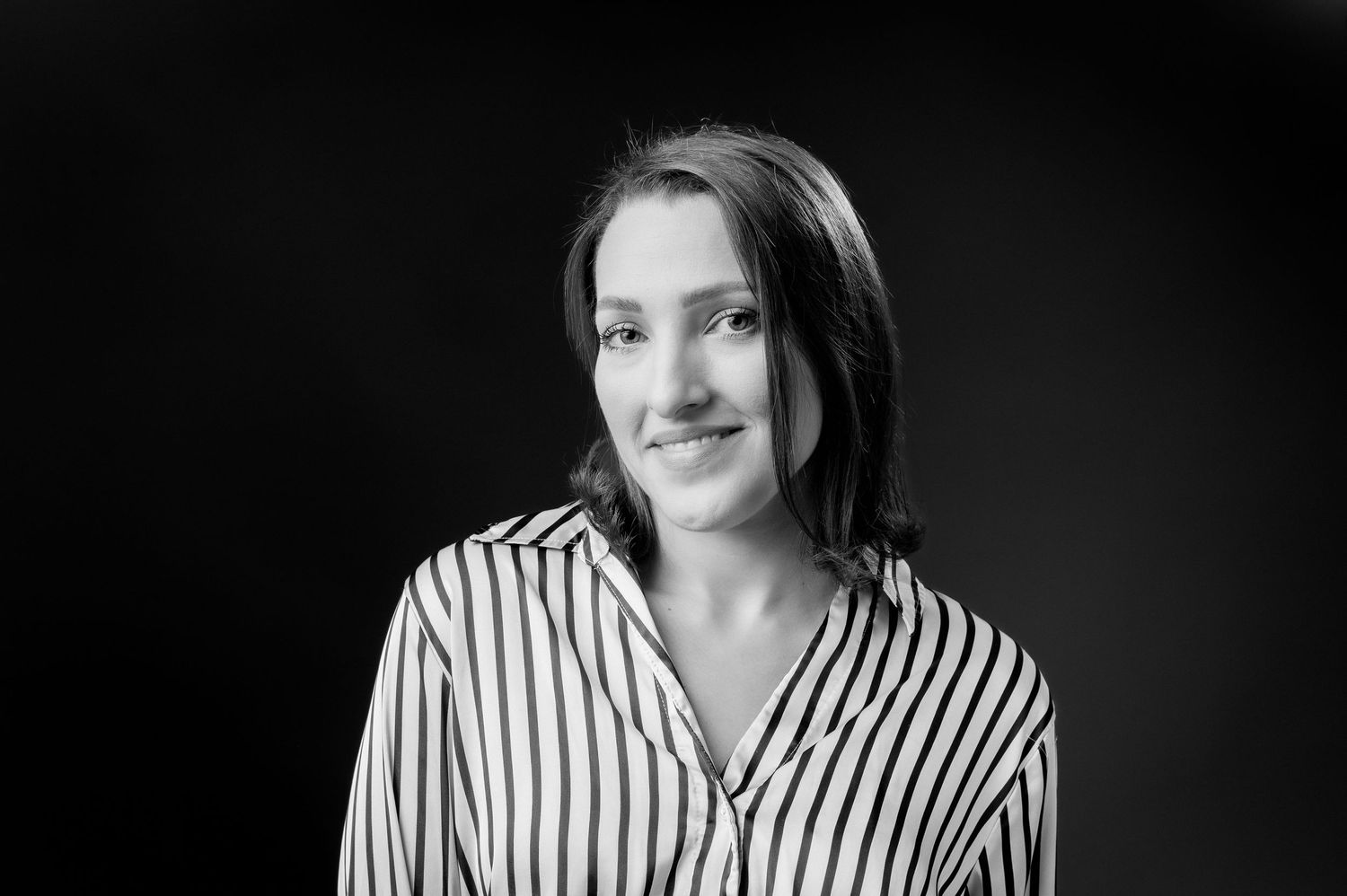 Black and white portrait of someone wearing a striped collared shirt against a dark background.