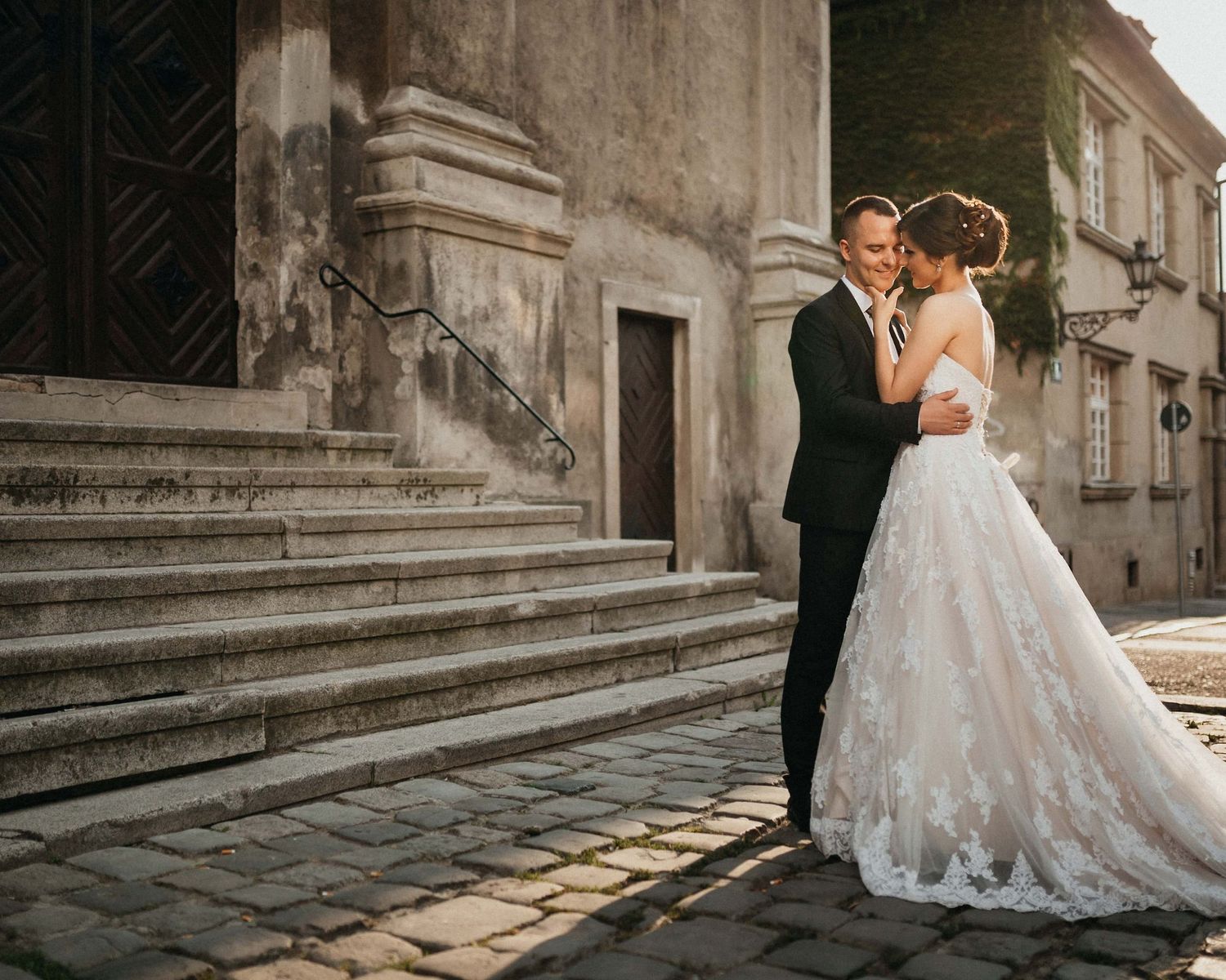 Romantic wedding couple embracing on vintage stone steps in European city setting.