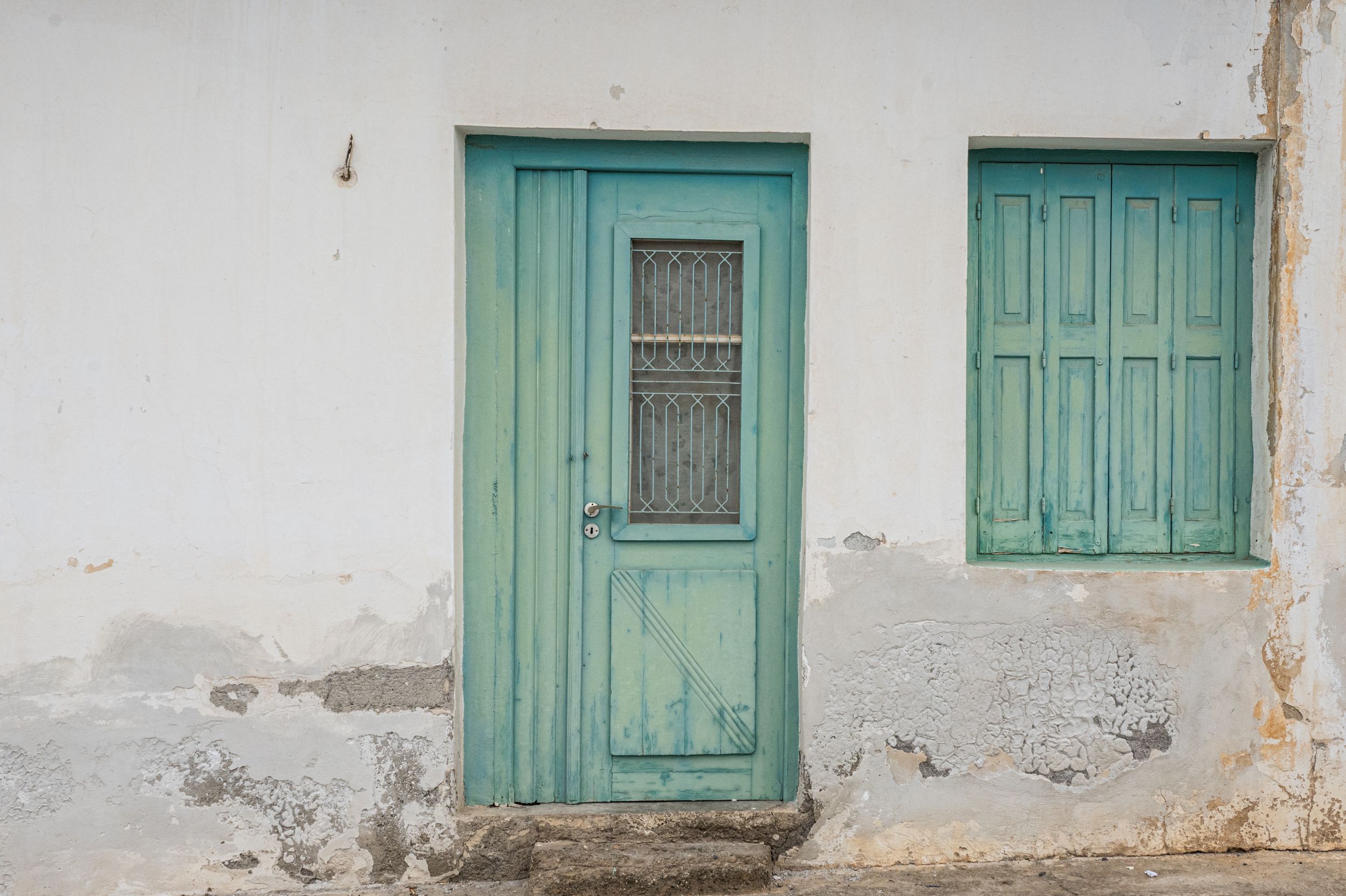 Weathered turquoise door and window on white stucco wall with peeling paint texture.