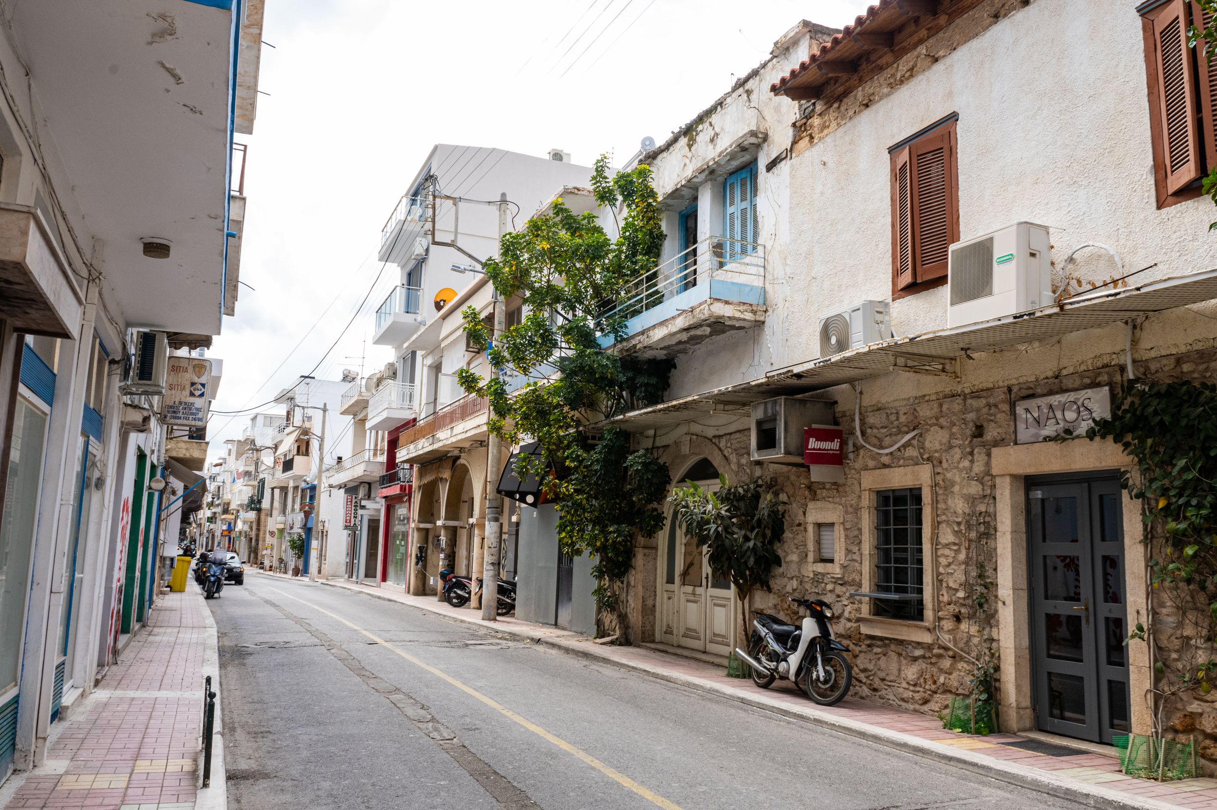 Narrow cobblestone street with traditional white buildings and blue shutters in a Mediterranean coastal town.