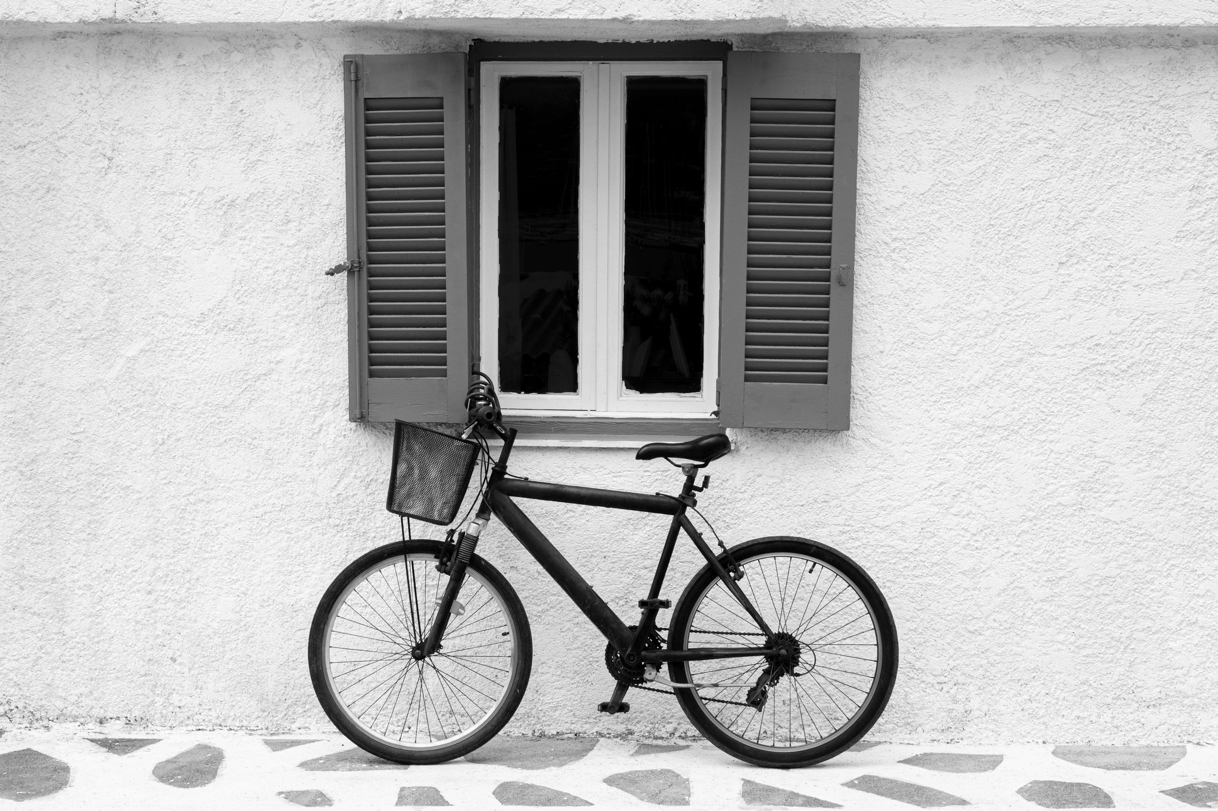 A black bicycle leans against a white stucco wall with gray shuttered windows creating a minimalist composition.