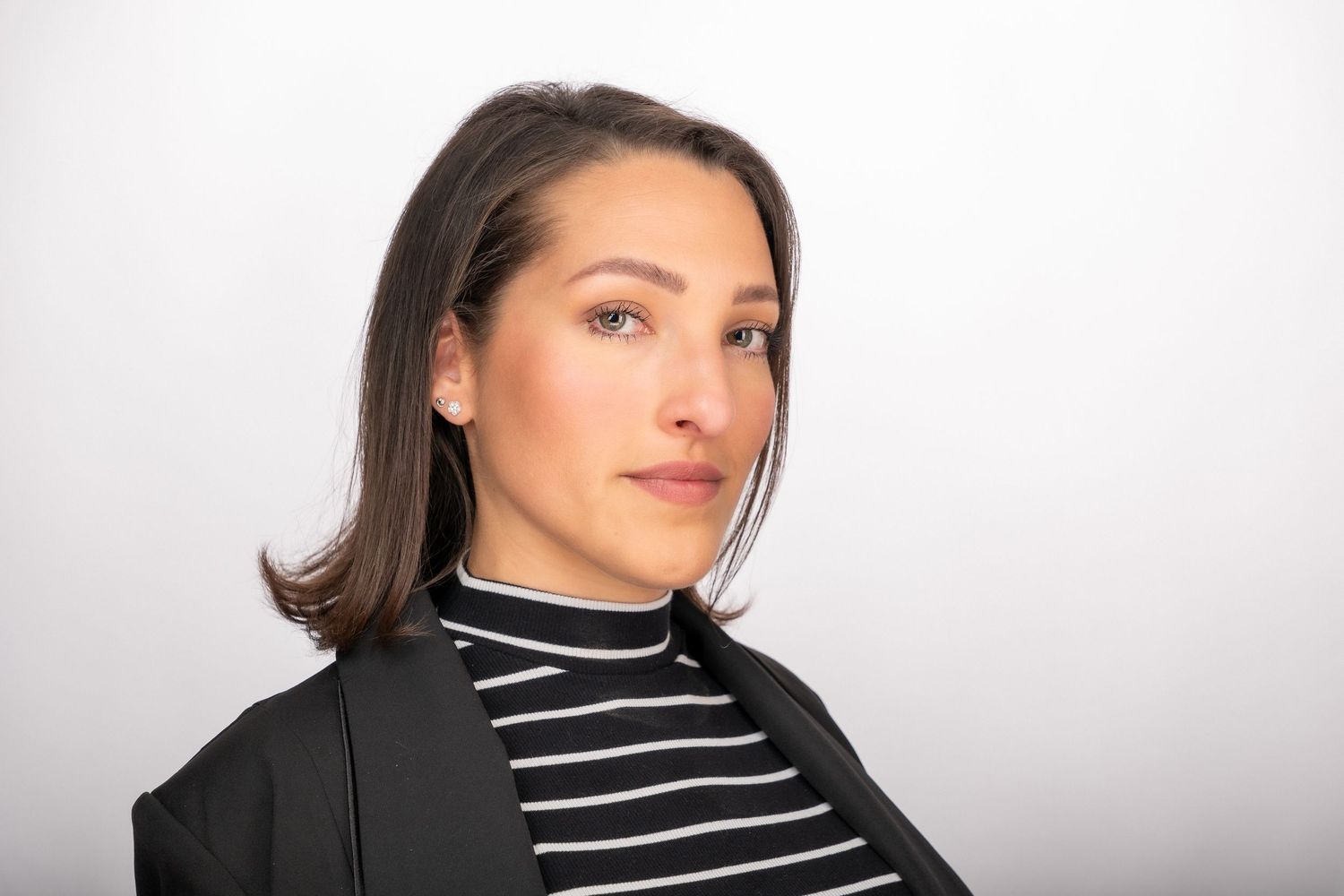 Professional portrait of someone wearing a black blazer and striped turtleneck against a light background.
