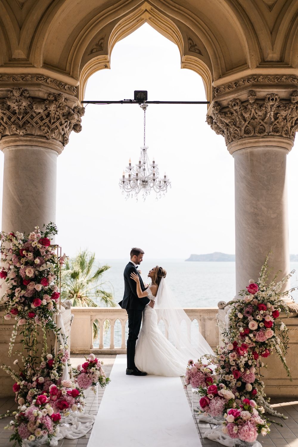 Bride and groom portrait at the loggia of Isola del Garda with glass chandelier decor and colorful floral decorations