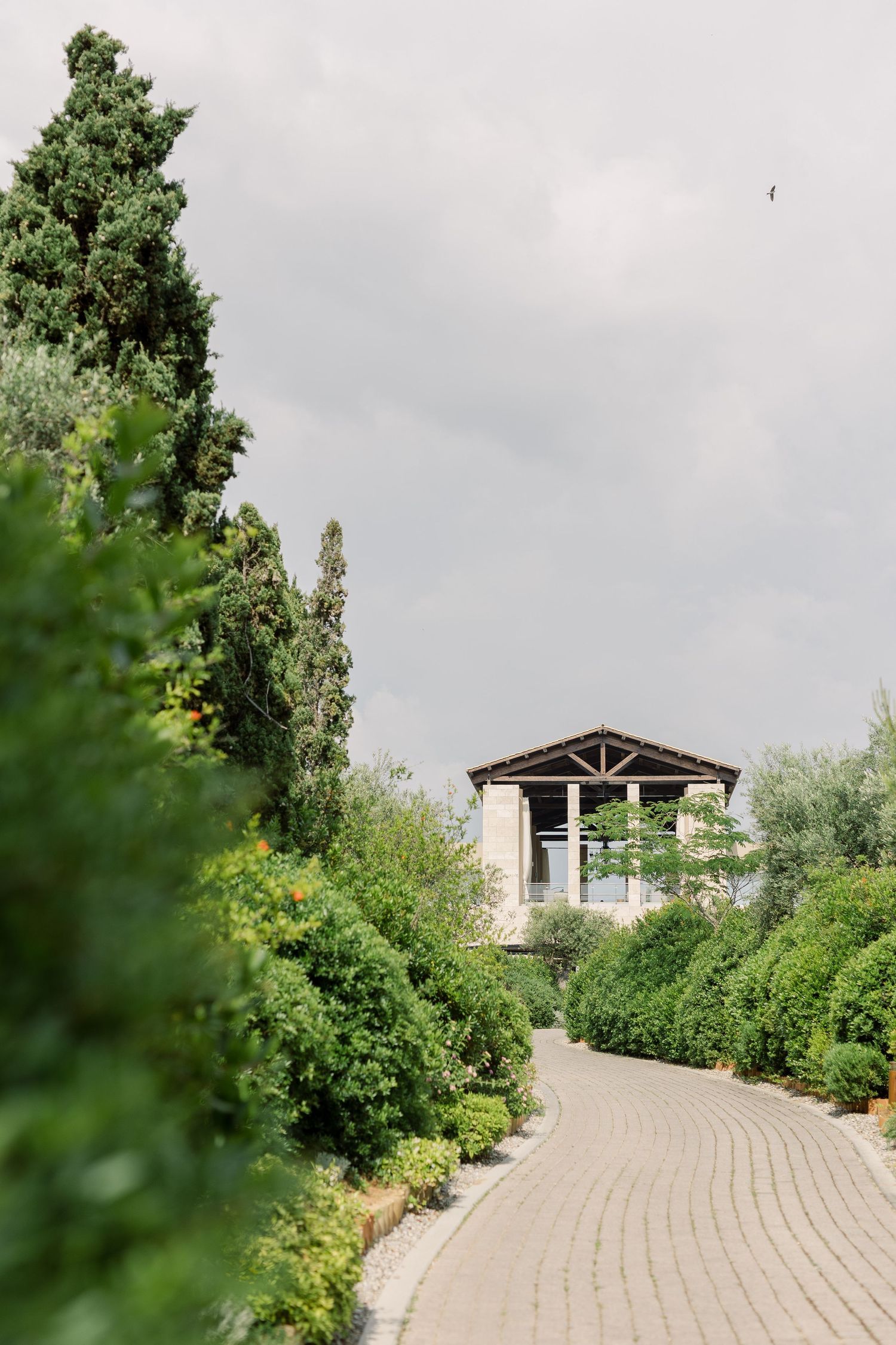 A winding stone path leads to a rustic wooden gazebo surrounded by lush green gardens and trees.