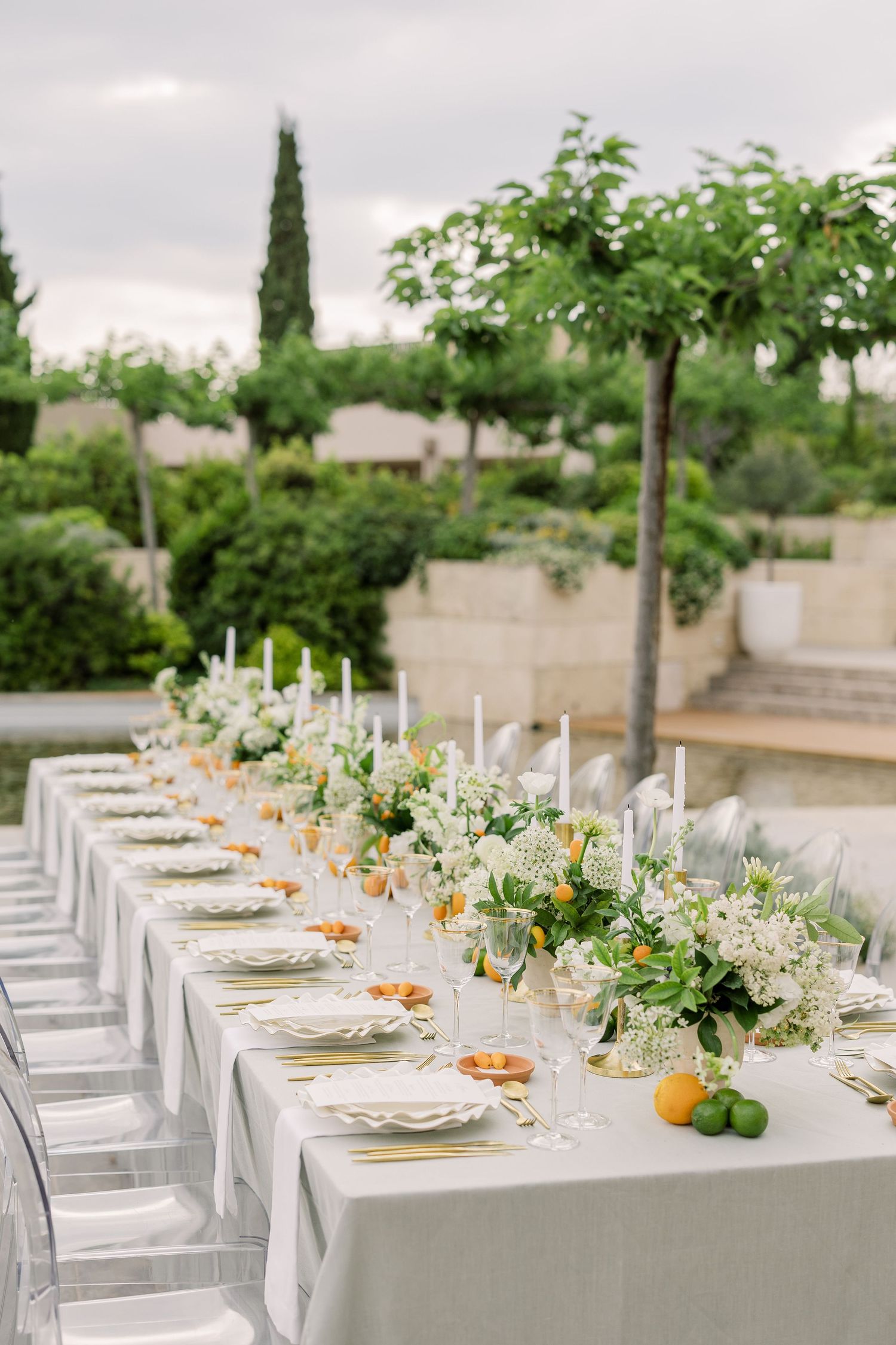 Elegant outdoor wedding reception table setting with white linens, fresh citrus accents and floral centerpieces.