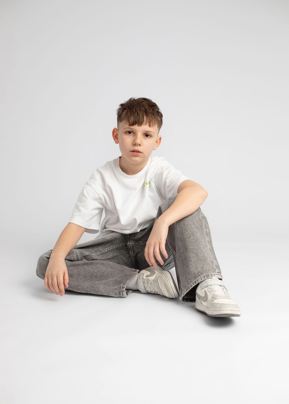 A person in a white t-shirt and gray pants lounges in relaxed poses against a light studio backdrop.
