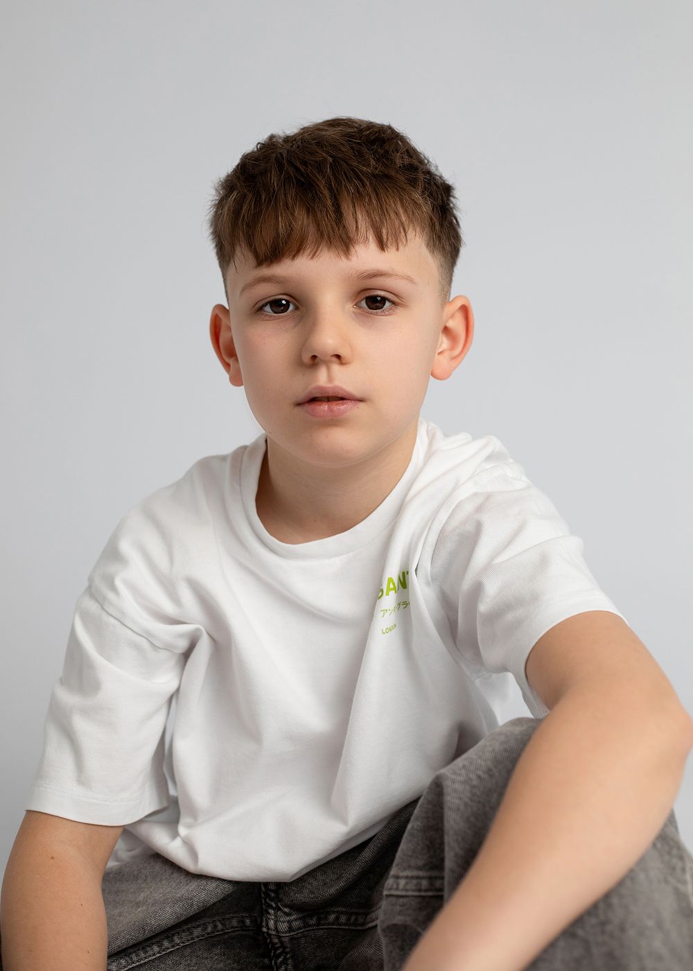 A child in a white t-shirt and jeans sits on a gray surface in a series of casual poses.