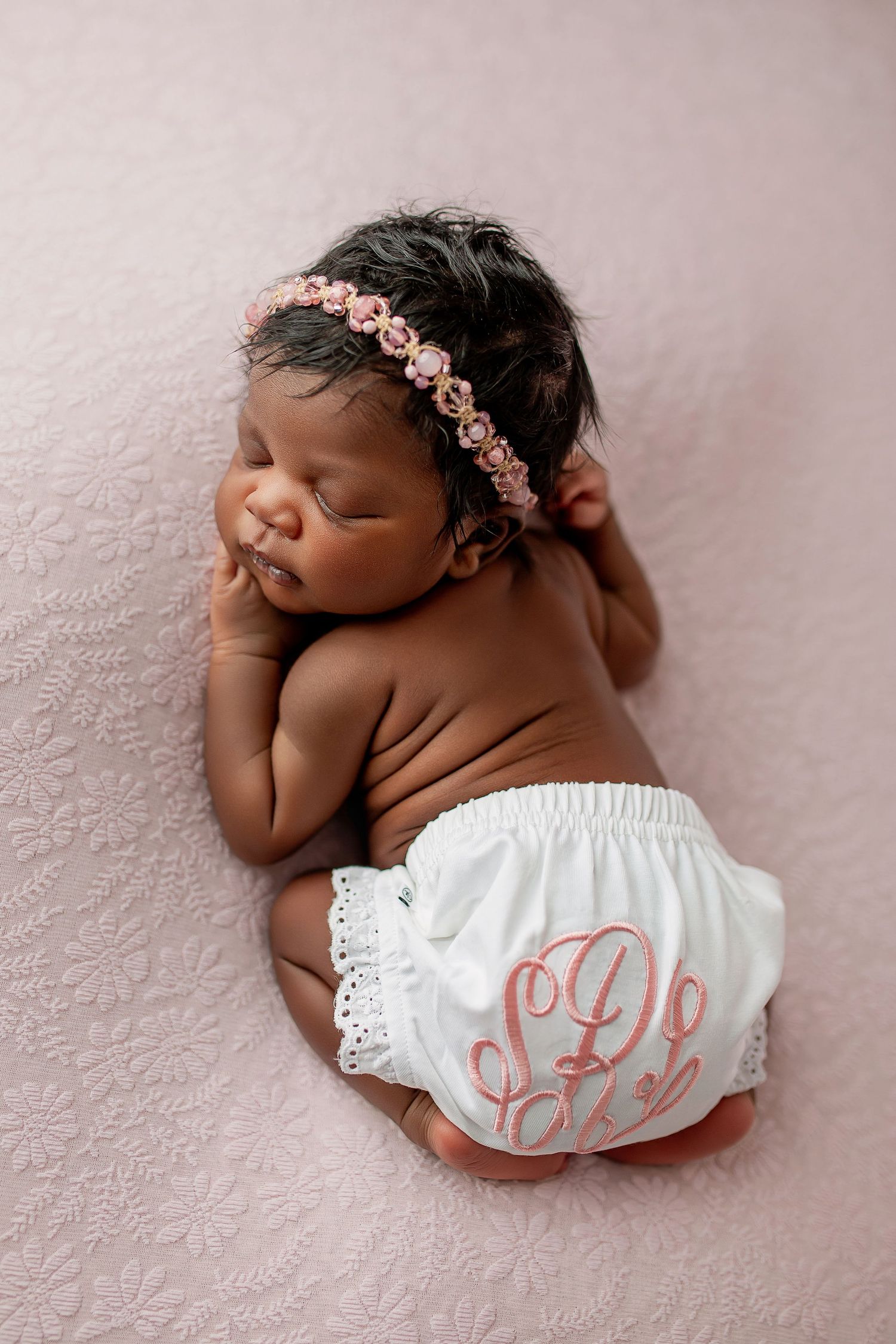 Newborn baby girl in purple bonnet and wrap sleeping in wooden basket on rustic wood floor