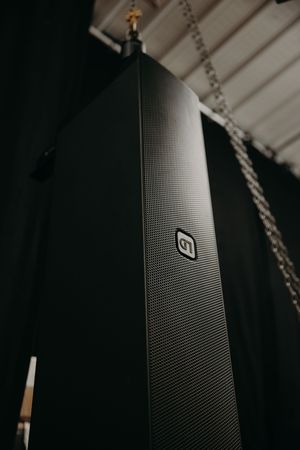 Professional black speaker array mounted on ceiling with industrial hardware in dark venue.