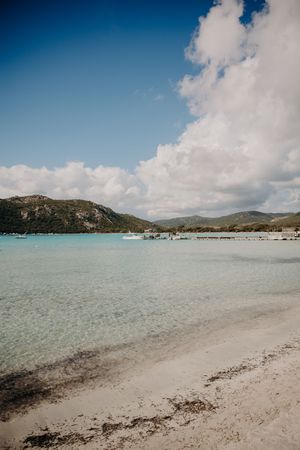 Pristine beach landscape with turquoise waters, mountains, and boats in the distance.
