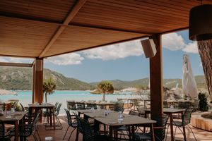Seaside restaurant terrace with mountain and ocean views under wooden roof.