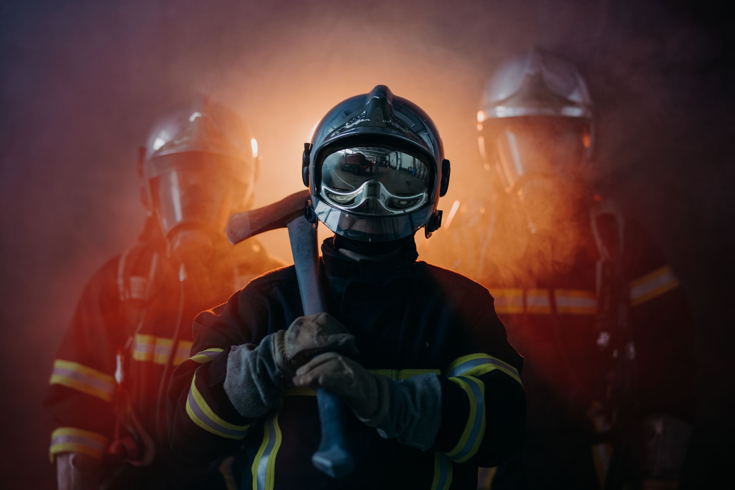 Firefighters in protective gear silhouetted against orange emergency lighting.