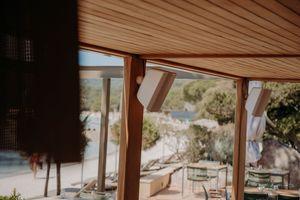 Interior view of a wooden-beamed structure with windows overlooking a coastal landscape.
