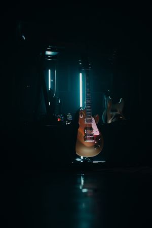 Electric guitar illuminated by blue lighting against dark background in moody studio setting.