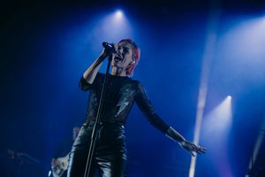 Concert performer singing on stage with dramatic blue lighting and fog effects.