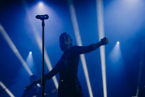 Silhouetted performer with arms raised on stage against blue spotlights.
