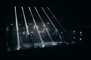 Concert stage lit by parallel white spotlight beams creating dramatic atmosphere.
