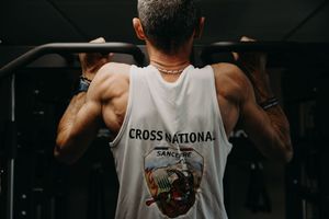 Athletic figures in white tank tops shown from behind in dark setting.