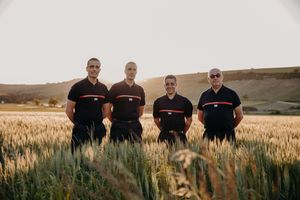Four people in matching black outfits stand together in a golden wheat field during sunset.