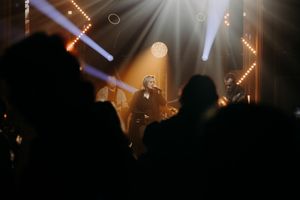 Concert lighting effects creating dramatic beams through atmospheric haze above crowd silhouettes.
