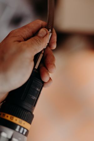 Hand holding a black power drill or screwdriver against a soft focus background.