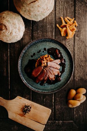 Dark plated dish with mushrooms and meat served on rustic wooden table.