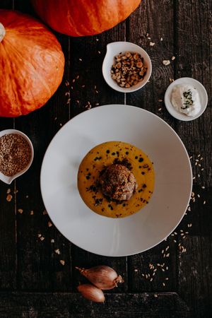 Orange pumpkin with creamy soup and dark garnish served on white plate.