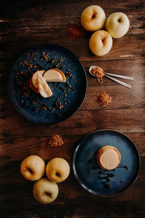 Yellow apples and dark plates arranged on wooden surface with scattered spices.