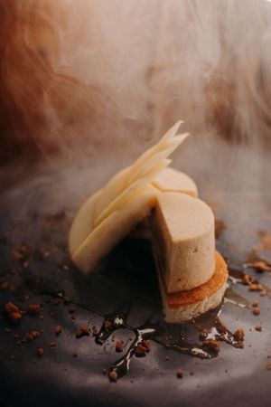 Layered dessert with steam effect and crumbs on dark surface.