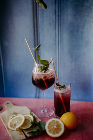 Cocktails with mint garnish and lemon slices against blue wall background.