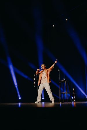Performer in beige outfit on stage with dramatic blue spotlights during stand-up comedy show.
