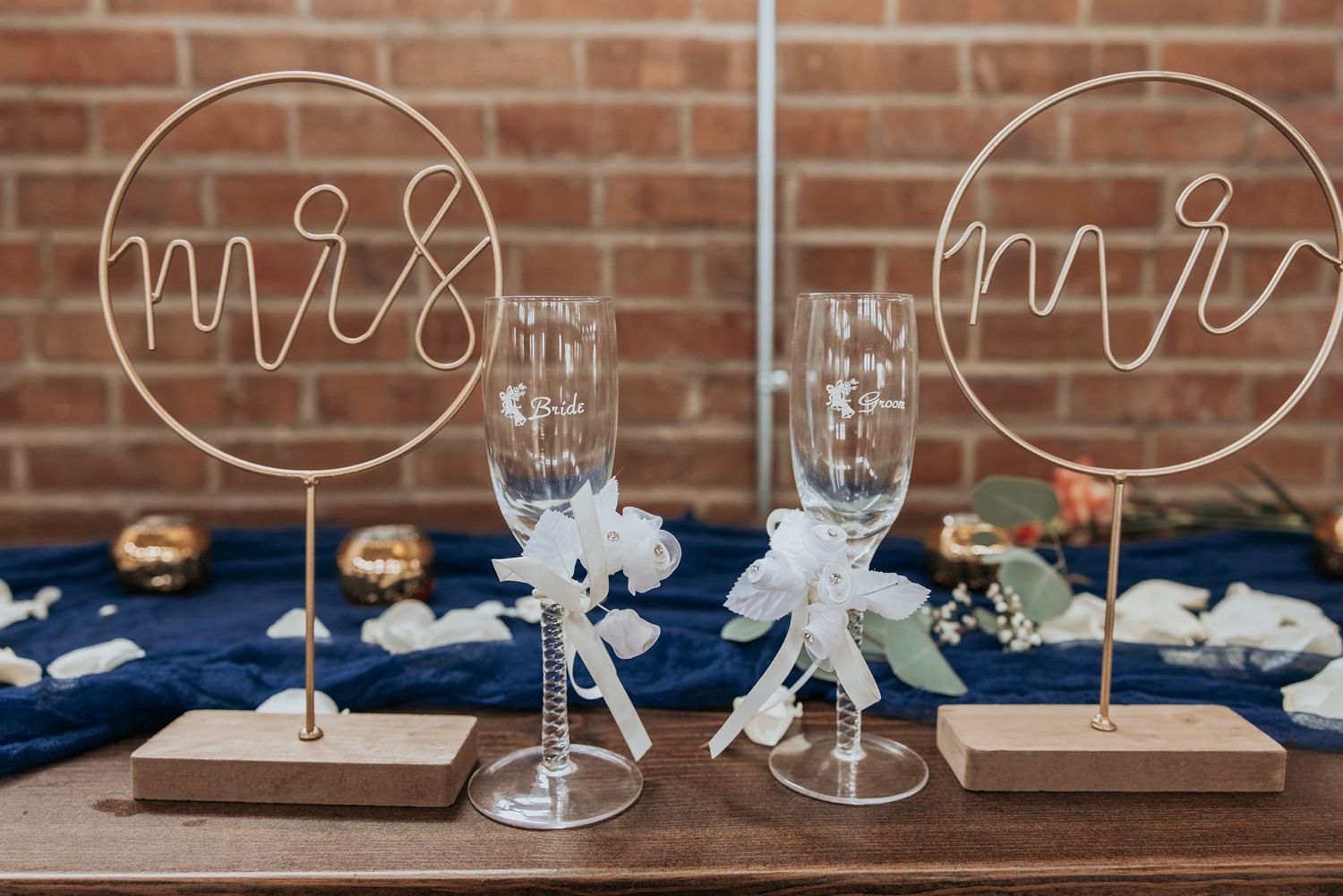 Clear acrylic signs with elegant calligraphy displayed on a brick wall with white floral decorations.