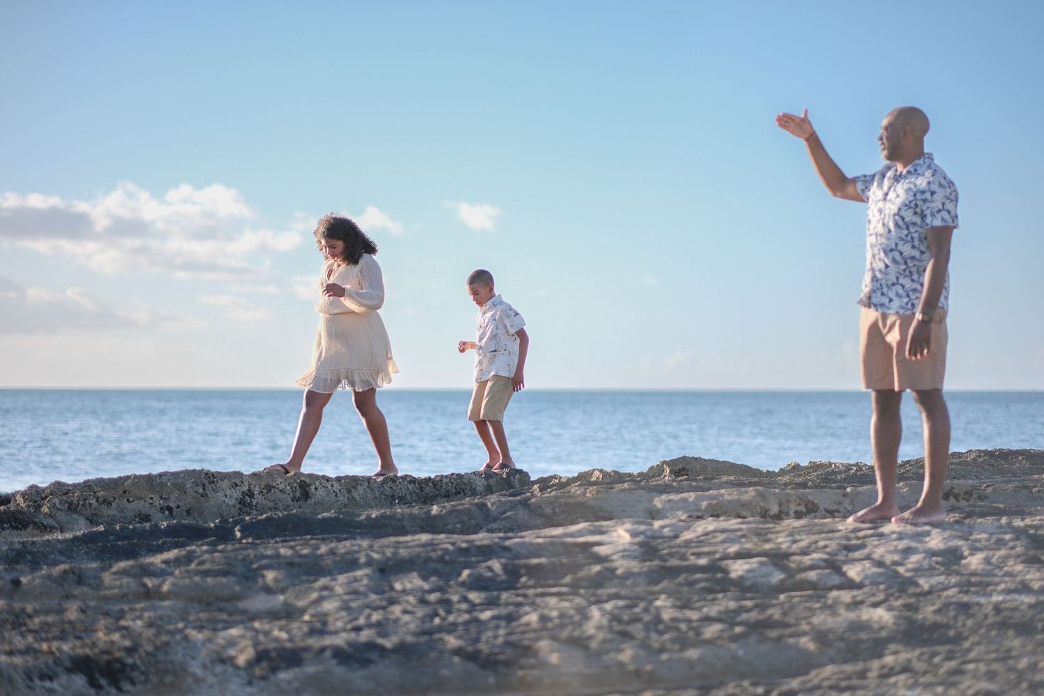 People exploring rocky coastal terrain with ocean waves and blue sky in the background.