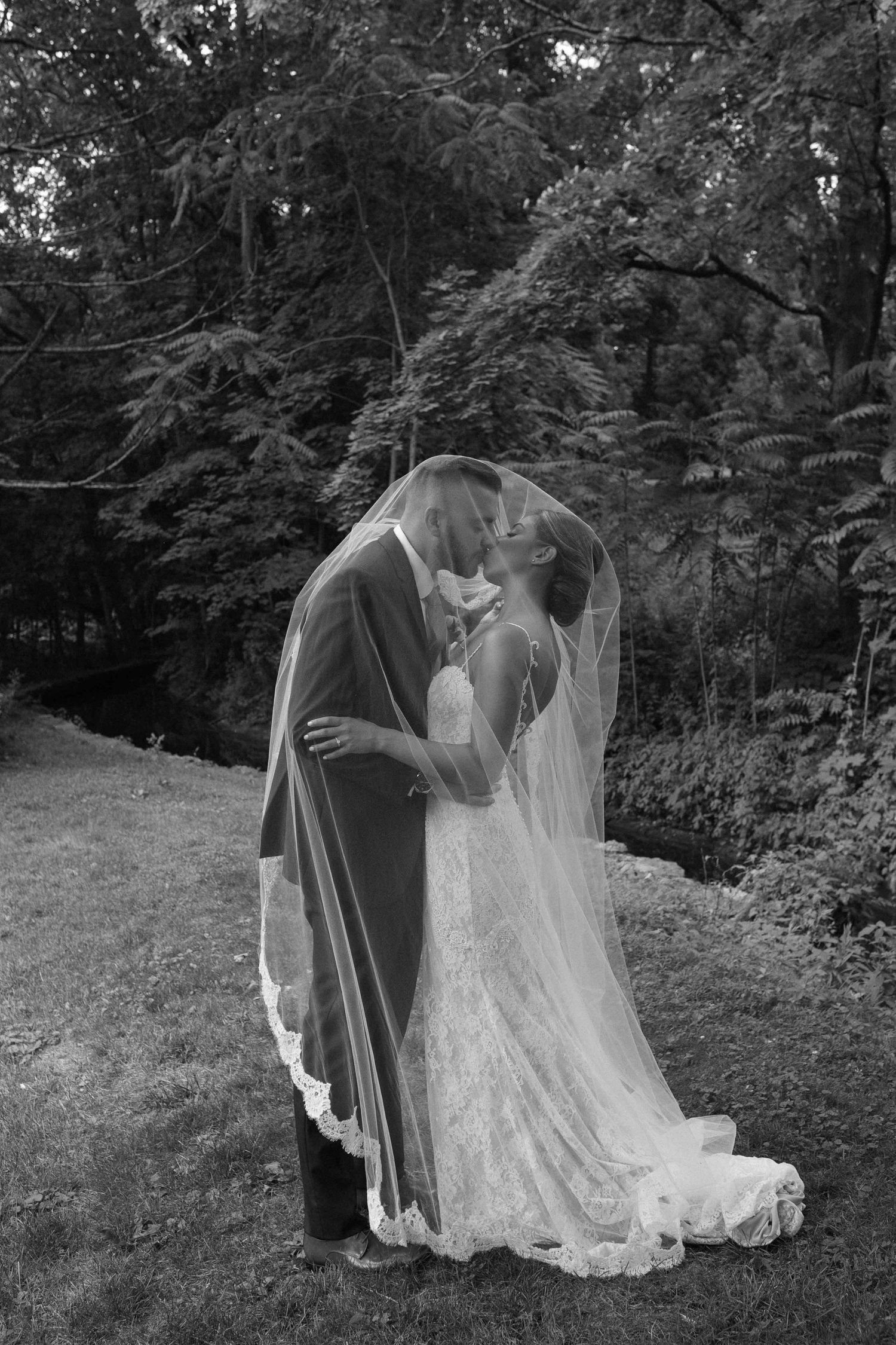 A romantic black and white photograph of a veiled couple sharing an intimate kiss on their wedding day.