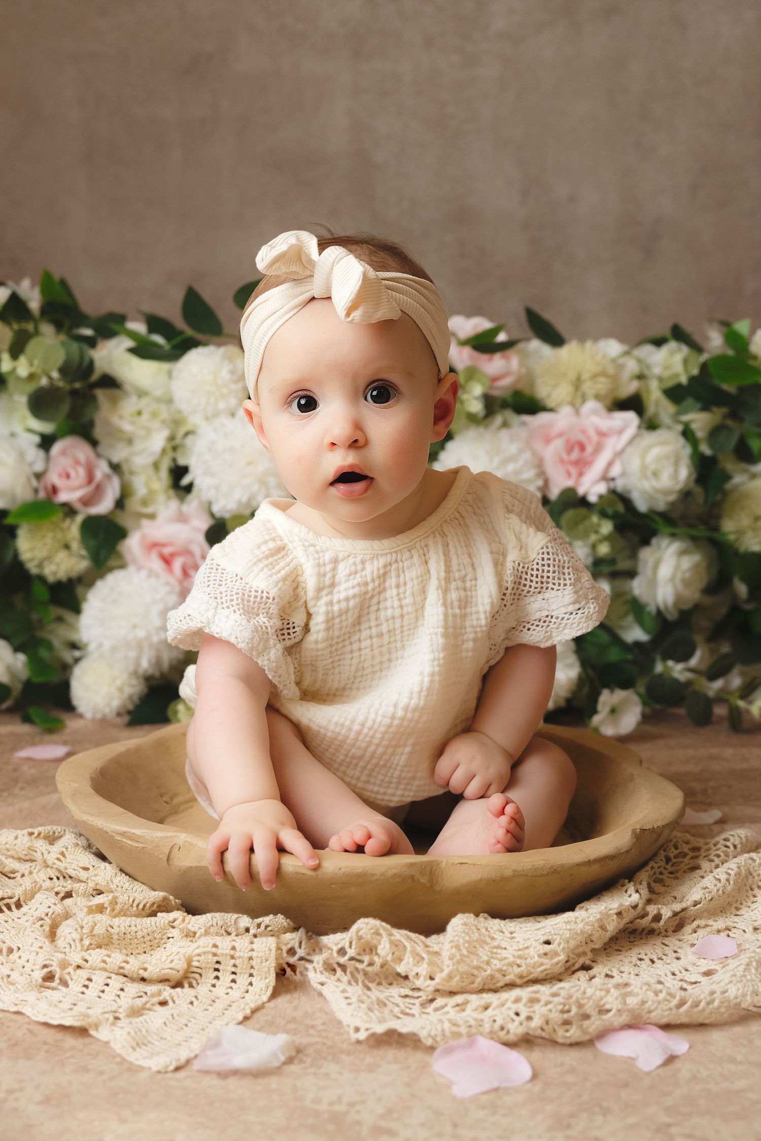 Adorable baby sitting in a wooden crate on a green backdrop, looking up curiously in a professional photo shoot.