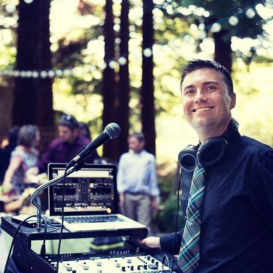 DJ at outdoor event working professional audio equipment with mixing board and sound system in natural setting.