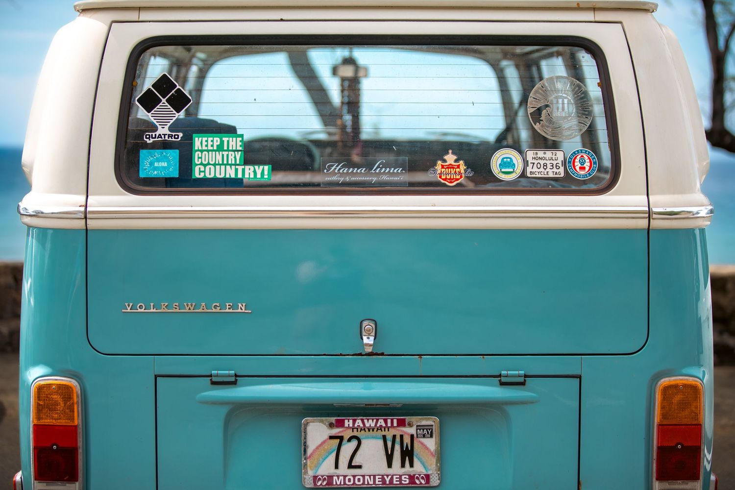 Vintage teal Volkswagen van with Hawaii license plate and travel stickers on rear window.