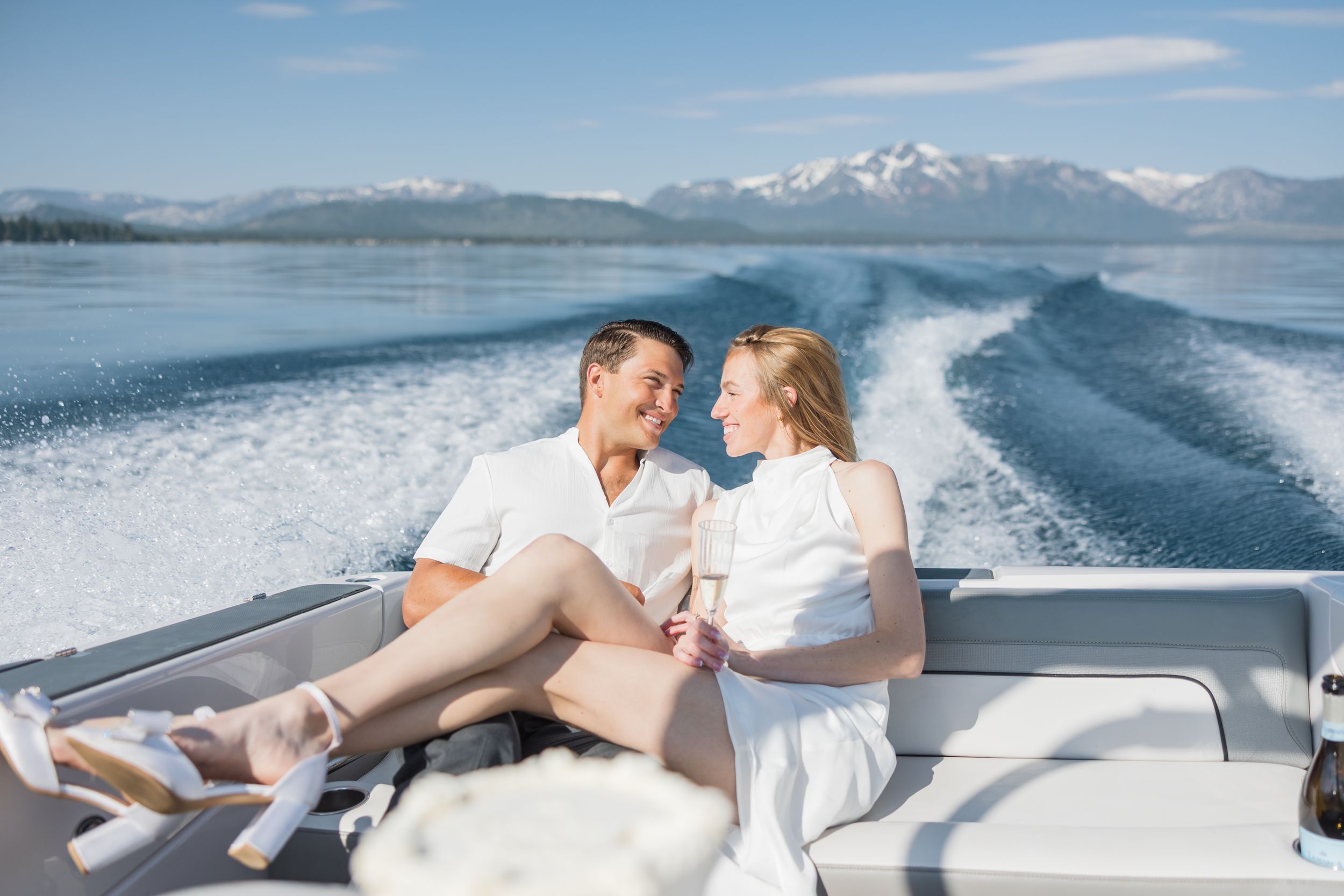 Couple sitting together on the back of a speedboat on a sunny day with mountain lake views.